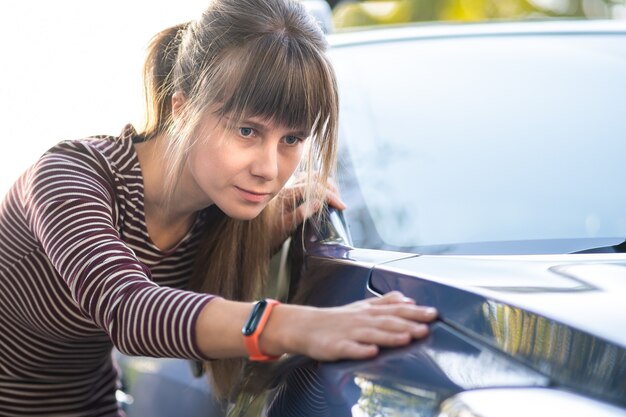 Junge Frau, die vor dem Kauf ein neues Auto im Verkaufsladen des Händlers untersucht.