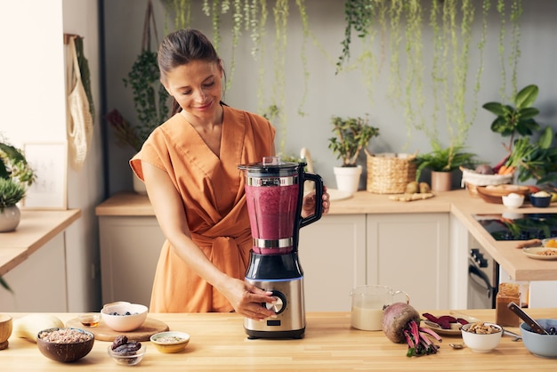 Junge Frau, die während des Kochens den Startknopf des Mixers drückt