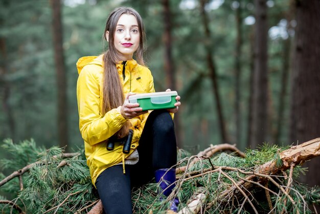 Junge Frau, die während des Reisens im Wald einen Snack mit gesundem Essen in der Lunchbox isst