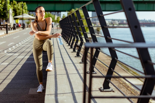 Junge Frau, die während des Trainings an der Flusspromenade eine Pause macht