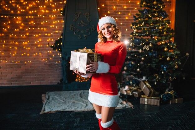 Junge Frau, die Weihnachtsgeschenke nahe beleuchtetem Baum auspackt. Weihnachten, Neujahrsfeierkonzept.