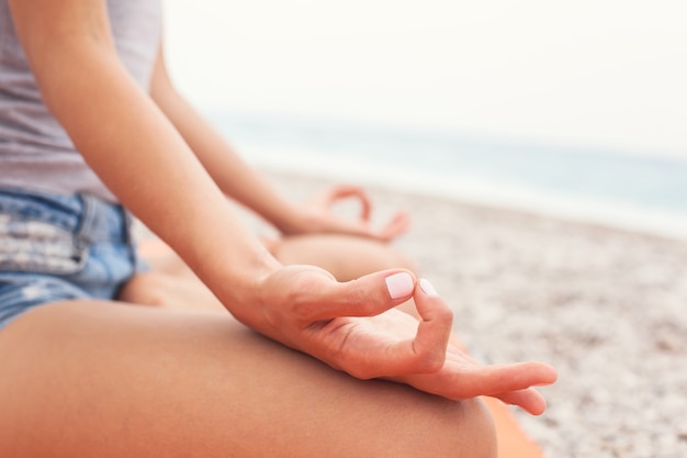 Junge Frau, die Yoga am Strand praktiziert, Nahaufnahme von Händen Gyan Mudra und Lotusposition