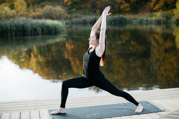 Junge Frau, die Yoga asana in der Natur nahe dem See tut