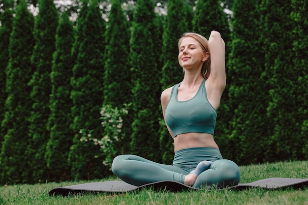 Junge Frau, die Yoga auf dem Gras im Garten praktiziert