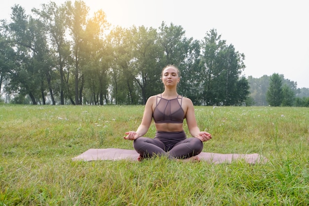 Junge Frau, die Yoga auf Matte im Sommerpark tut. Gesundes Sport-Lifestyle-Konzept. Aktive und sportliche Frauenübungen