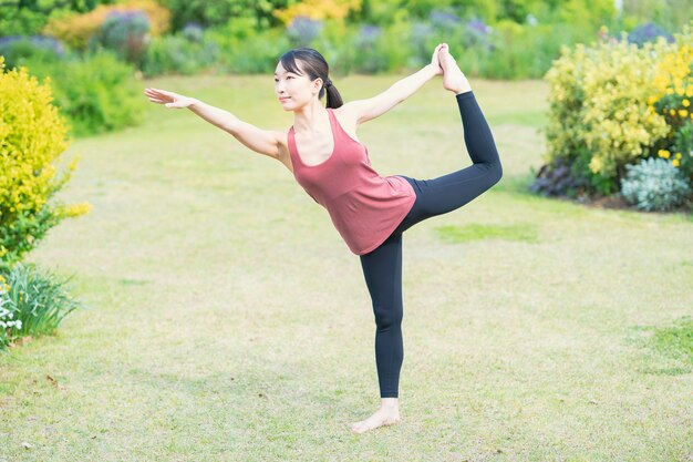 Junge Frau, die Yoga in einem grünen Park am schönen Tag tut