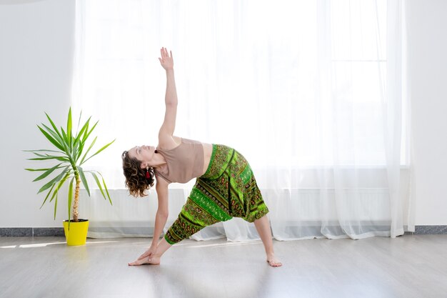 Junge Frau, die Yoga praktiziert, steht in Utthita Trikonasana Übung mit erweiterter Dreieckshaltung