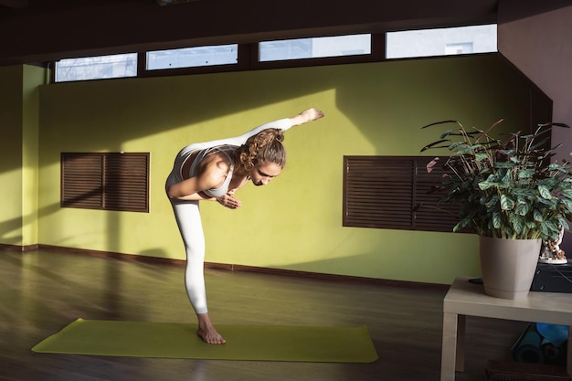 Junge Frau, die Yoga praktiziert und eine Variation der Adhomukha Uthitahasta Padangushthasana-Übung macht