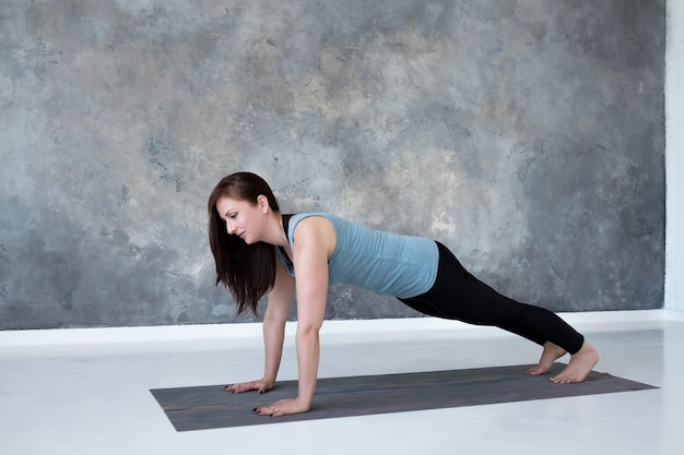 Junge Frau, die Yoga praktiziert und Liegestütze oder Liegestütze macht, trainiert Plank-Pose
