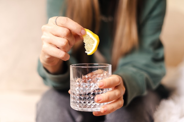 Junge Frau, die Zitronenscheibe und Glas Wasser, Nahaufnahme hält