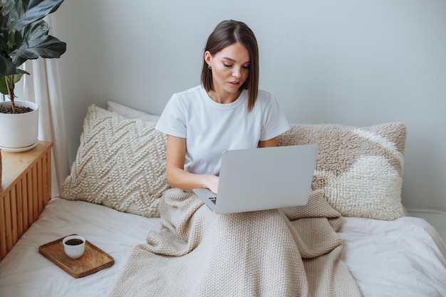 Junge Frau, die zu Hause am Laptop im Bett arbeitet