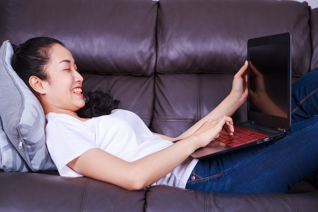 junge Frau, die zu Hause eine Laptop-Computer auf Sofa im Wohnzimmer verwendet