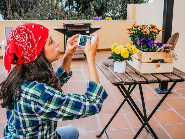 Junge Frau, die zu Hause im Garten arbeitet und Fotos zu Blumen macht