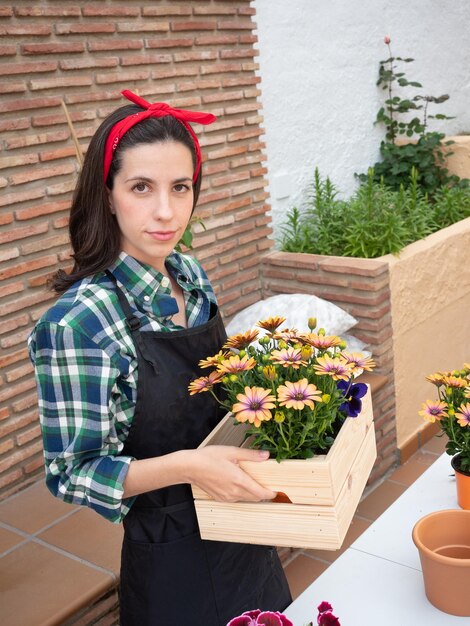 Junge Frau, die zu Hause mit Holzkiste und Pflanzen im Garten arbeitet