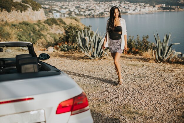 Junge Frau, die zum Cabrioletauto am Meer geht