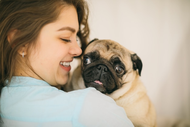 Junge Frau, die zum kleinen Pughund schauend lächelt