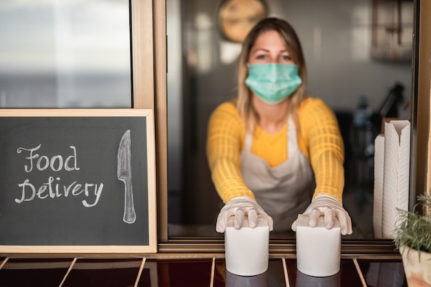 Junge Frau, die Zustellungsnahrung im Restaurant zum Mitnehmen während der Coronavirus-Ausbruchsperiode vorbereitet - Arbeiter innerhalb der Küche, die gesundes Essen für Hausbestelldienst kocht