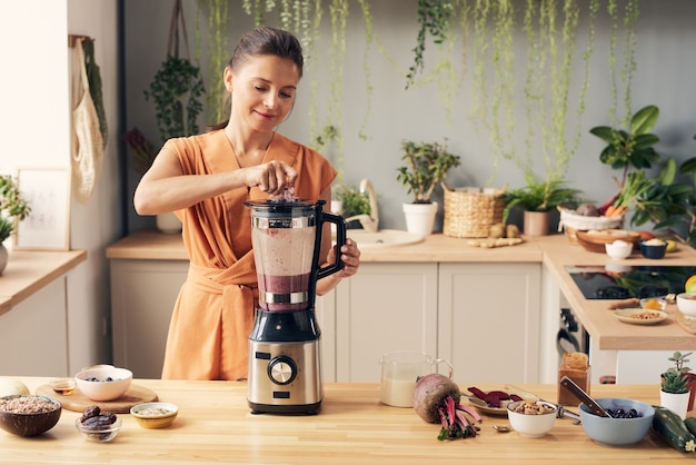 Junge frau, die zutaten von smoothie im elektrischen mixer mischt