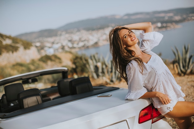 junge Frau durch weißes Cabrioletauto an einem sonnigen Sommertag