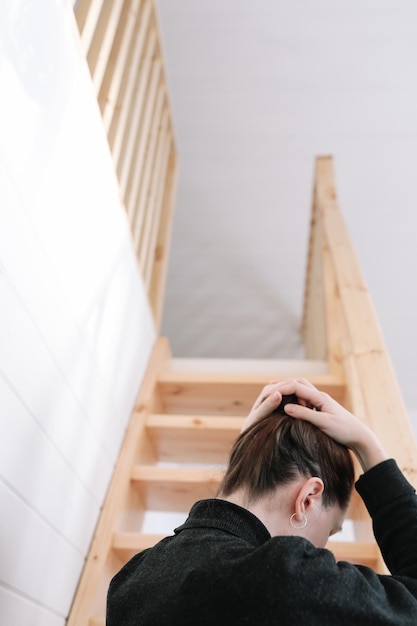 Junge Frau einfache Frisur Rückansicht durch Holztreppe zu Hause Depression Einsamkeit und Quarantänekonzept Psychische Gesundheit Selbstversorgung zu Hause bleiben