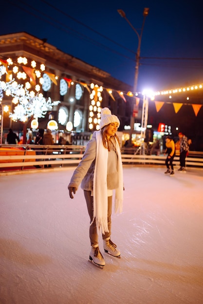 Junge Frau Eislaufen auf einer Eisbahn in einem festlichen Weihnachtsmarkt in den Abendlichtern herum