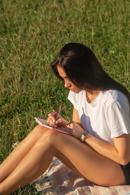 Junge Frau entspannt sich im Park und schreibt in ein Notizbuch