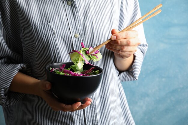 Junge Frau essen Salat mit Stäbchen auf Blau