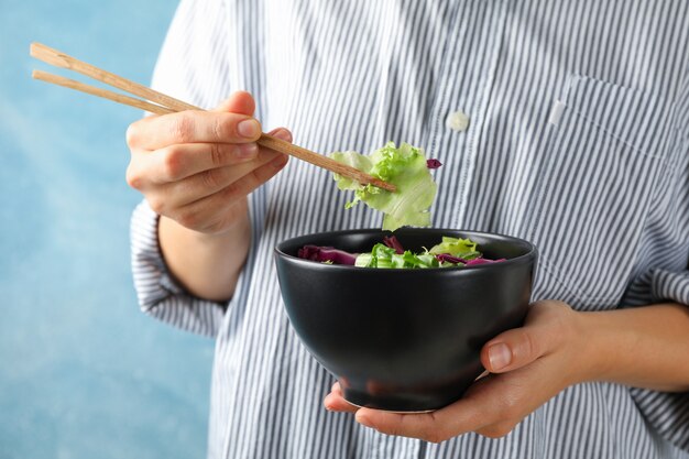 Junge Frau essen Salat mit Stäbchen auf Blau