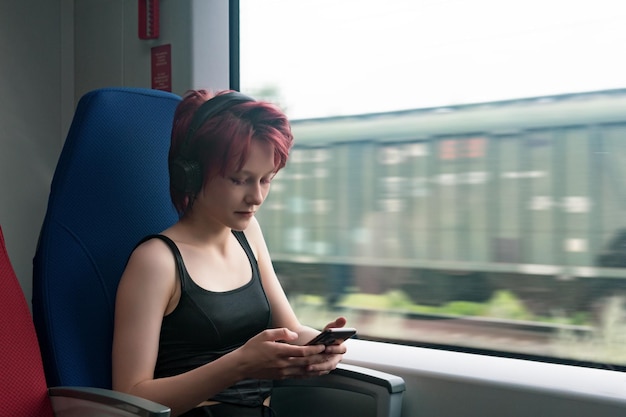Junge Frau fährt in einem Zug, der in ein Smartphone eingetaucht ist