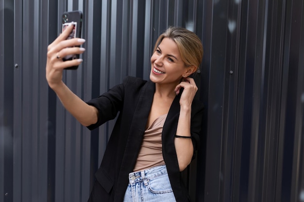 Junge Frau fotografiert sich am Telefon im Büro vor grauem Hintergrund