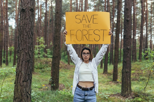 Junge Frau freiwillig in den Waldpfählen und hält ein Plakat, um den Wald zu retten