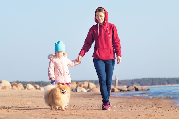 Junge Frau geht mit Mädchen und Hund am Strand.