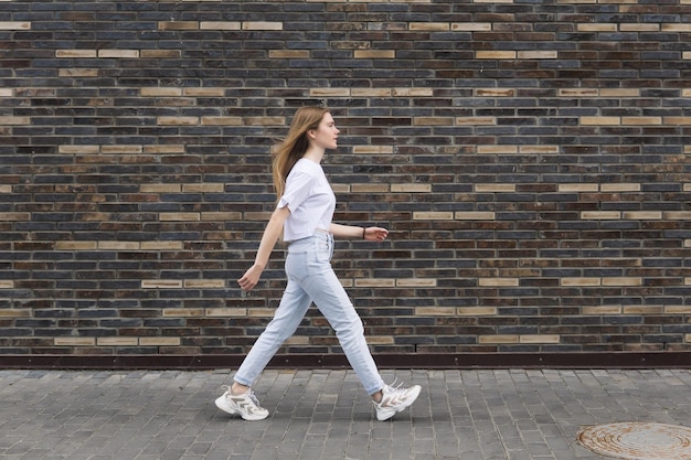 Junge Frau geht vor einer Ziegelmauer die Straße entlang