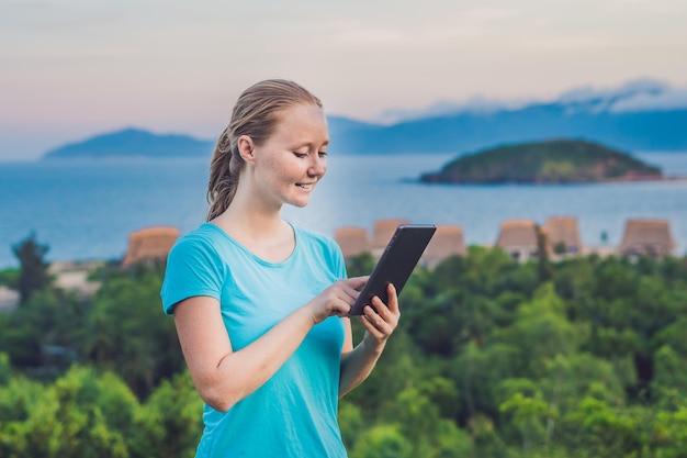 Junge Frau genießt eine Tablette auf dem Hintergrund des Meeres.