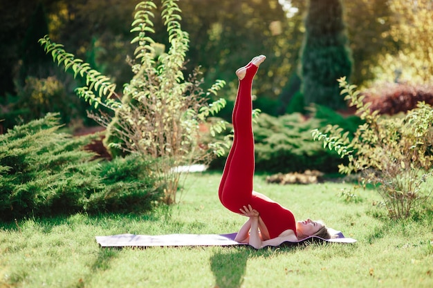 Junge Frau genießt Meditation und Yoga auf grünem Gras im Sommer auf dem Kopf stehend