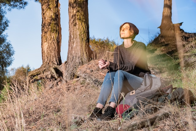 Junge Frau genießt schönes Herbstwetter. Wandererin sitzt an einem sonnigen Nachmittag unter Kiefern