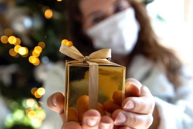 Junge Frau gibt goldene Geschenkbox, die eine schützende Gesichtsmaske für Covid-19 trägt