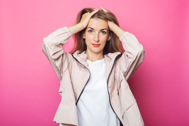 Junge Frau glättet ihr Haar in einer rosa Jacke, rosa isolierten Hintergrund.