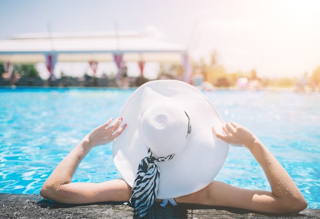 Junge Frau glücklich im großen Hut, der auf dem Schwimmbad entspannt