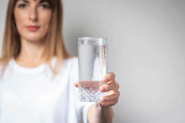 Junge Frau hält ein Glas mit klarem Wasser auf einer hellen Oberfläche