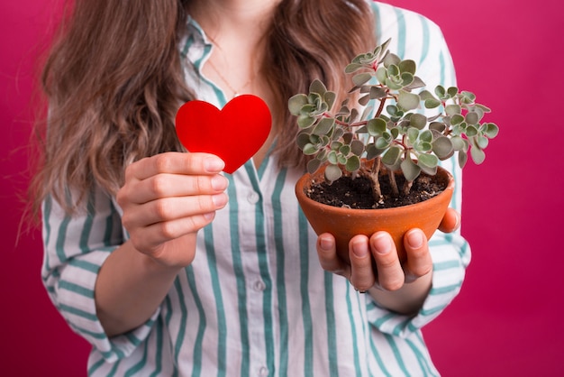 Junge Frau hält ein rotes Herz für die Liebe und eine Topfpflanze