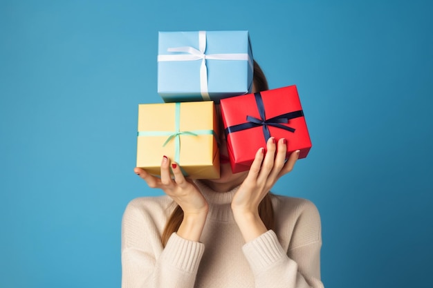 Junge Frau hält einen Stapel Geschenkboxen vor ihrem Gesicht vor blauem Studiohintergrund