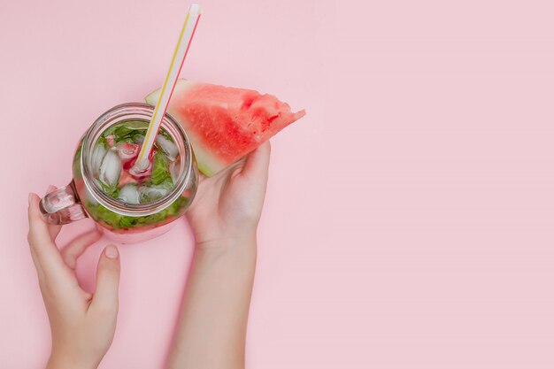 Junge Frau hält frisch gepresste Wassermelonenlimonade von Zitrusfrüchten. Weibchen mit Einmachglas voll kaltem Cocktail, Minzblätter. Rosa Hintergrund, Kopierraum, Nahaufnahme