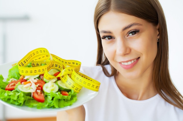 Junge Frau hält gesunden Salat mit grünen frischen Zutaten und gelbem Band.