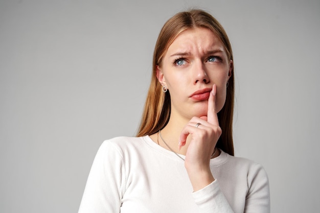 Junge Frau hält sich von Hand zu Gesicht auf grauem Hintergrund