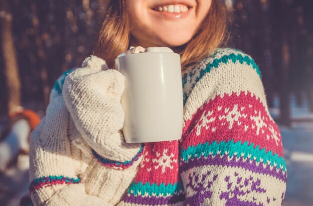 Junge Frau hält Tasse Kaffee mit Marshmallow im Winterwald