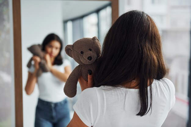 Junge Frau hält Teddybär und betrachtet sich im Spiegel