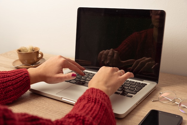 Junge Frau Hände auf Laptoptastatur auf Holztisch mit Kopierraum auf Computerbildschirm und Lichtwand und Büro Requisiten und Teetasse auf Schreibtisch