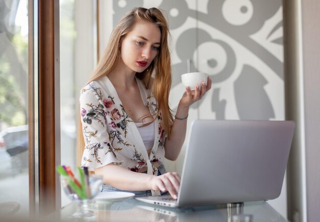 Junge Frau hat einen Videoanruf, während sie an einem Tisch mit einem Laptop sitzt