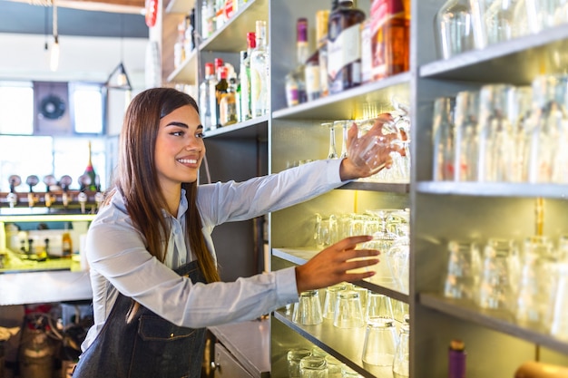 Junge Frau hinter der Bar, die ein sauberes Glas nimmt, um ein Getränk einzuschenken.